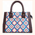A structured tote bag with a colorful geometric diamond pattern in blue, red, cream, and white, accented by dark brown faux-leather trim and handles.